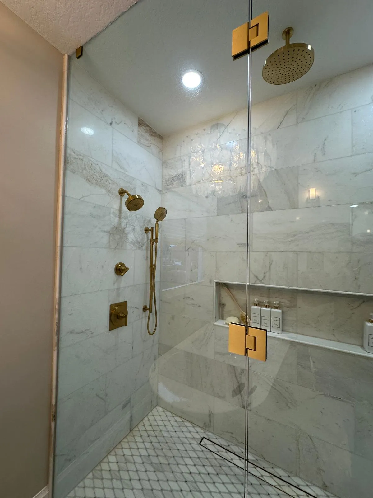 Glass walk-in shower with a rain shower head and marble-look tile, bathroom remodeling in Port St Lucie, FL